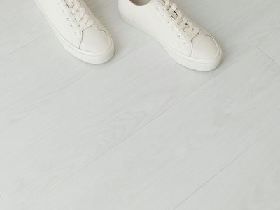 A pair of clean white sneakers on a wooden floor.